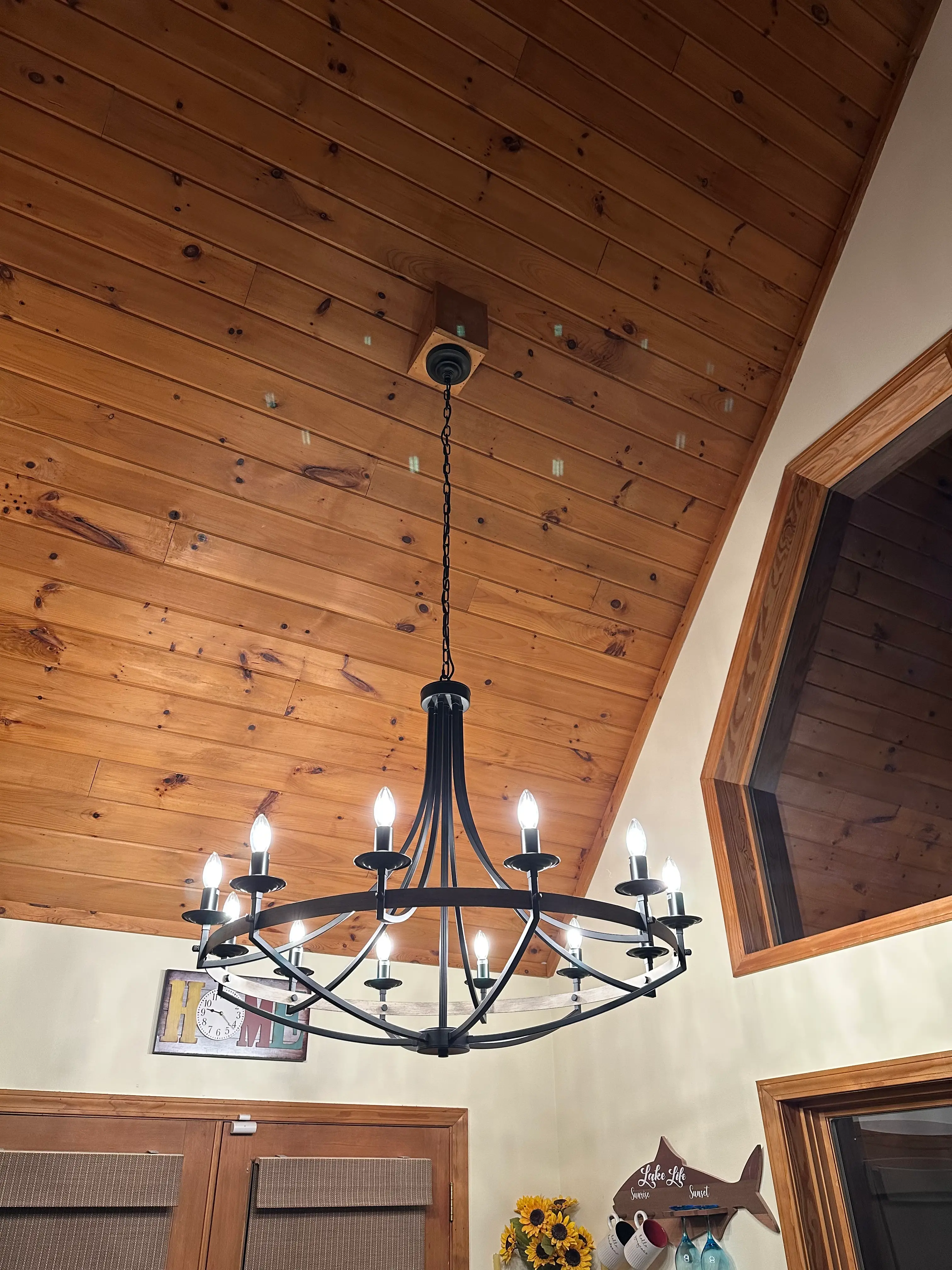Large black circular chandelier illuminated beneath a wood-paneled vaulted ceiling
